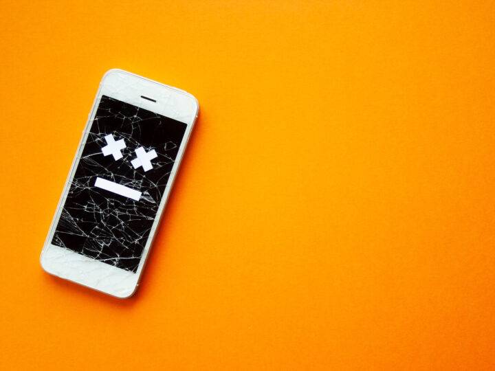 Kaputtes Smartphone mit zerbrochenem, zerstörtem Bildschirm und traurigem Lächeln, auf orangefarbenem Hintergrund