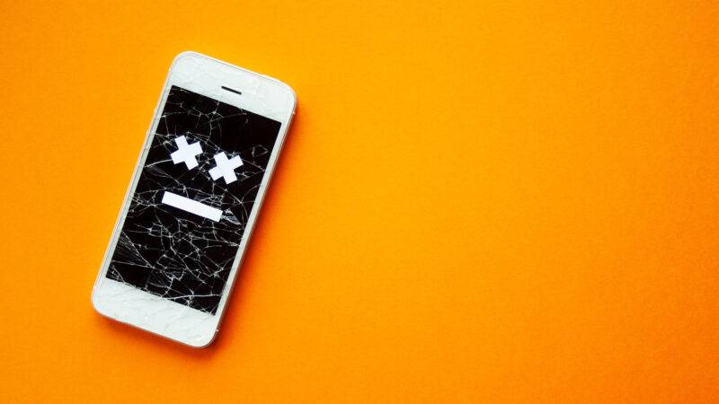 Kaputtes Smartphone mit zerbrochenem, zerstörtem Bildschirm und traurigem Lächeln, auf orangefarbenem Hintergrund