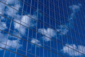 Der blaue Himmel und die weißen Wolken spiegeln sich in dem Glasgebäude.