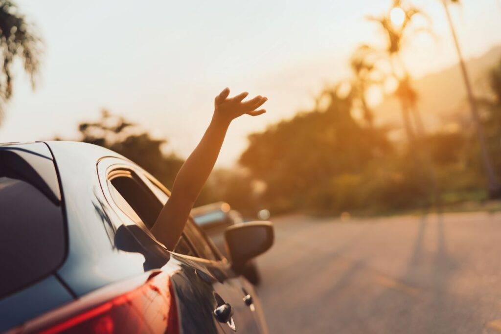 Hand streckt sich aus einem Autofenster in den Sonnenuntergang, symbolisch für die Freiheit eines Roadtrips mit Ausfuhrkennzeichen aus Mettmann.