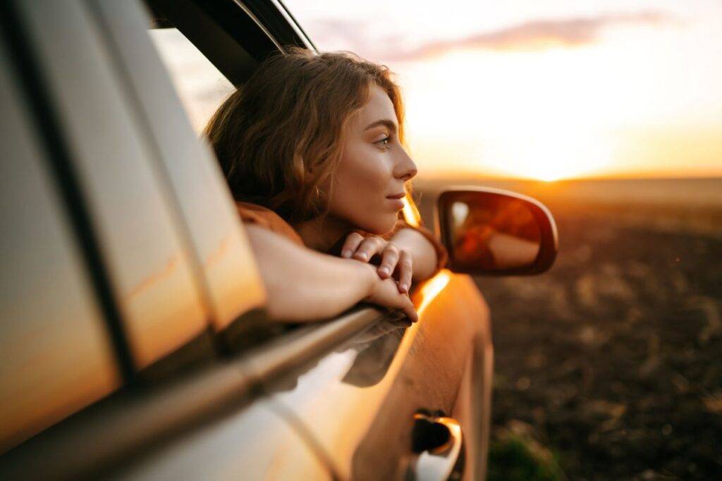 Frau lehnt aus dem Autofenster und genießt den Sonnenuntergang, bereit für eine Auslandsfahrt mit Ausfuhrkennzeichen aus Mettmann