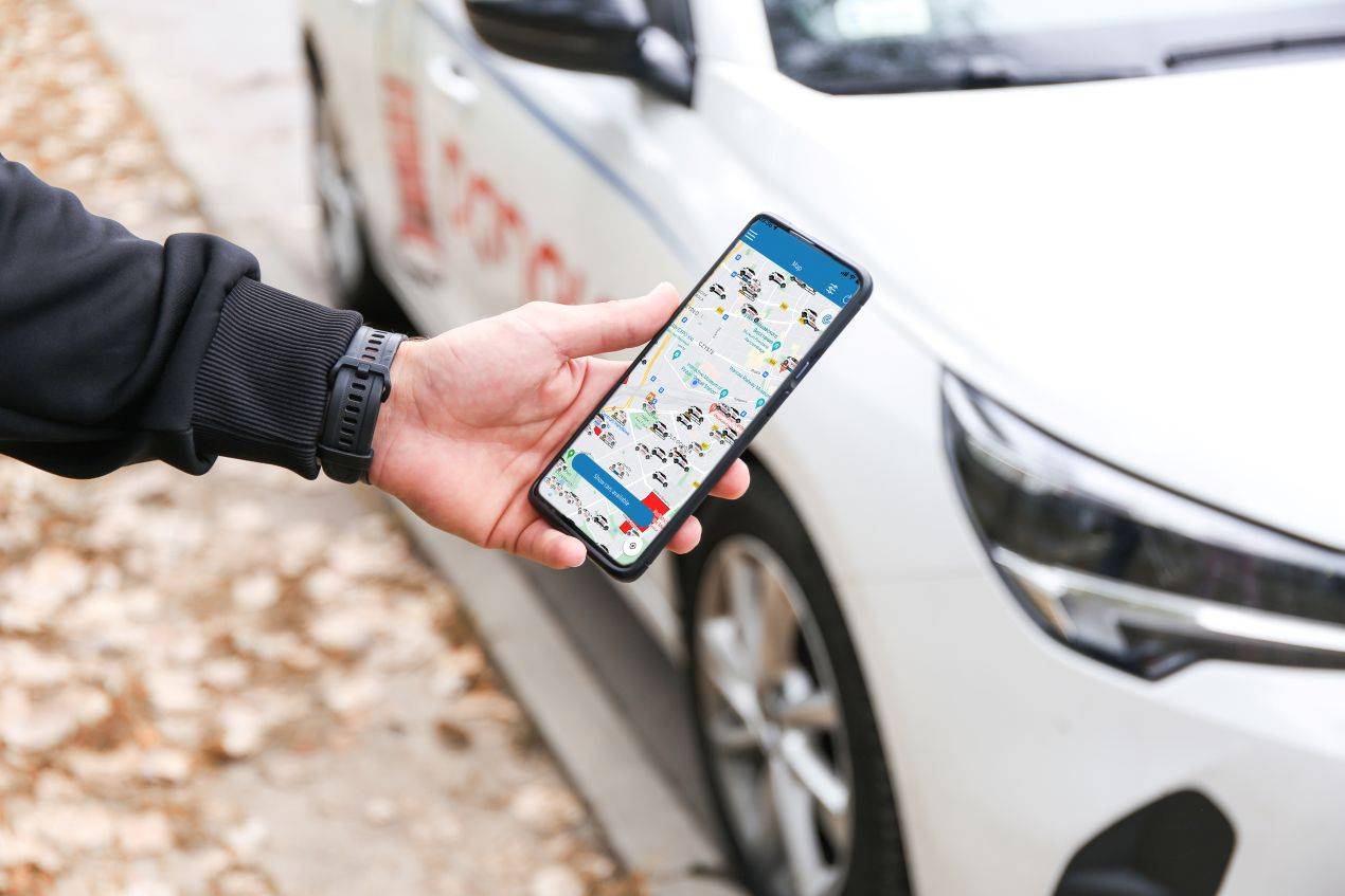 Hand hält ein Smartphone mit einer Carsharing-App vor einem geparkten Auto – WAB Schweiz und moderne Mobilitätskonzepte für Neulenker