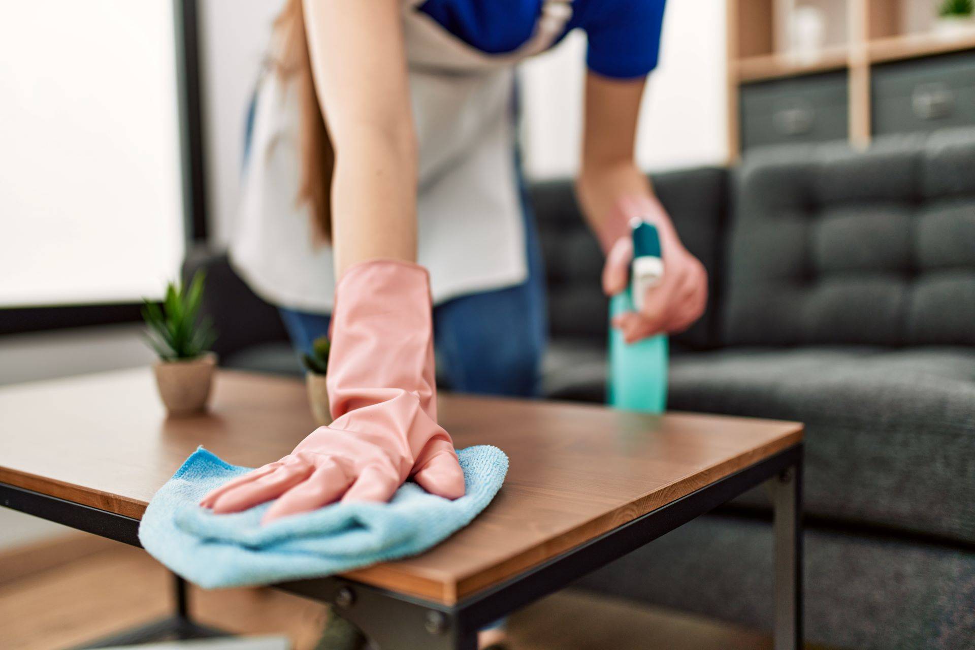 Hausangestellte reinigt Wohnzimmertisch mit Handschuhen